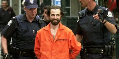 Steven-Guilbeault arrested an handcuffed by police wearing in orange Greenpeace jumpsuit