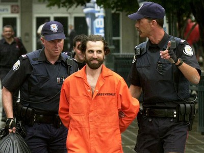 Steven-Guilbeault arrested an handcuffed by police wearing in orange Greenpeace jumpsuit